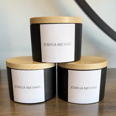 Three black candles with wooden lids and labels reading 'Joshua Michael'.