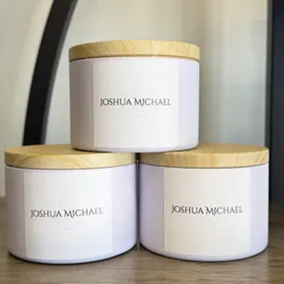 Three white candles with wooden lids labeled 'Joshua Michaels'.