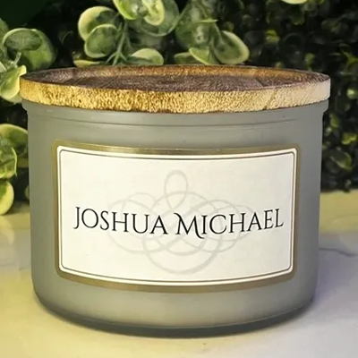 A scented candle in a frosted glass jar with a cork lid labeled Joshua Michael.