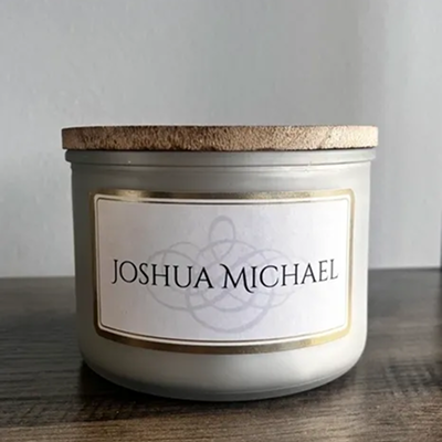 A white candle with a cork lid labeled 'Joshua Michael'.