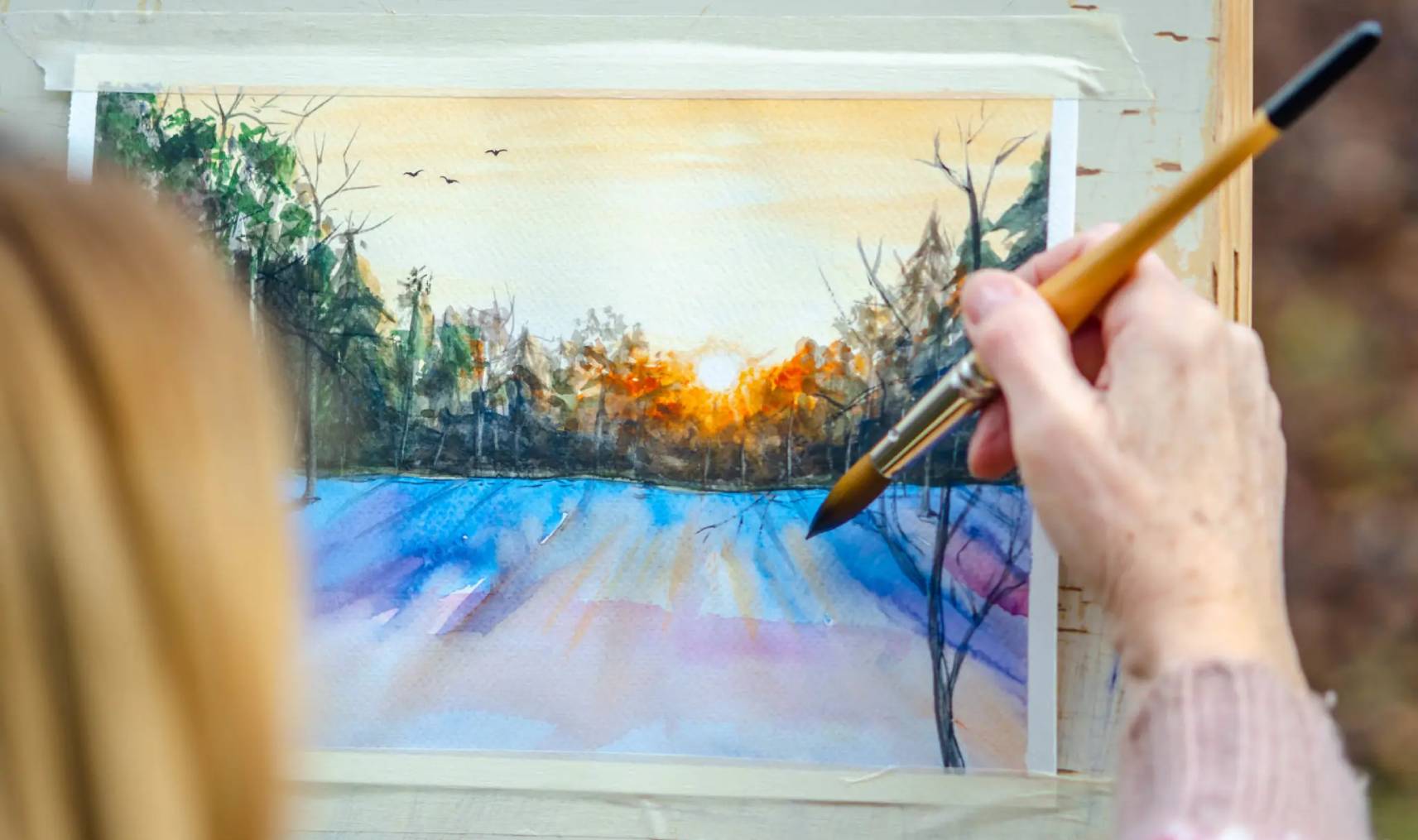Artist painting a sunset landscape with vibrant colors.