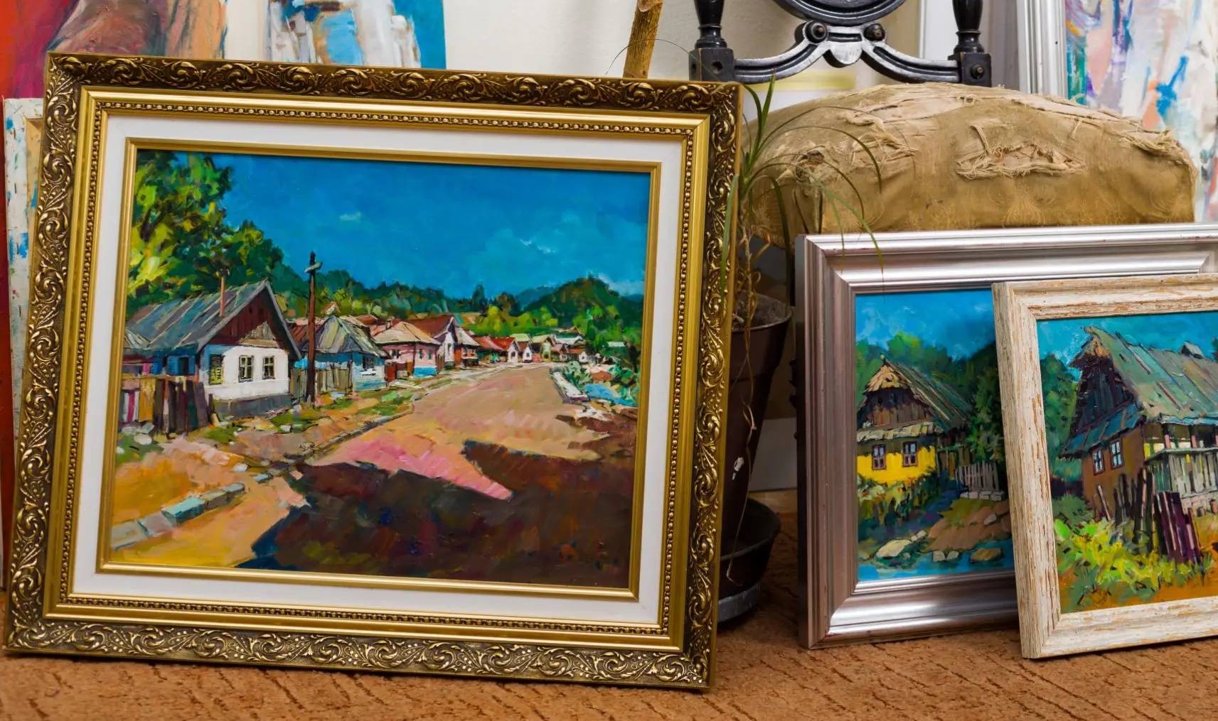 Two framed landscape paintings leaning against furniture indoors.