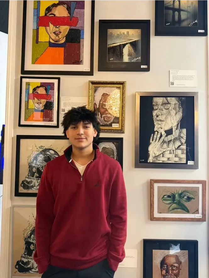 Young person standing in front of a wall with framed artwork.