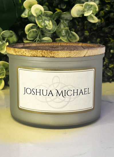 A scented candle with a cork lid labeled Joshua Michael.