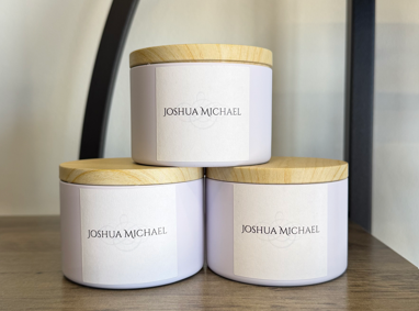 Three white candles with wooden lids labeled Joshua Michael.
